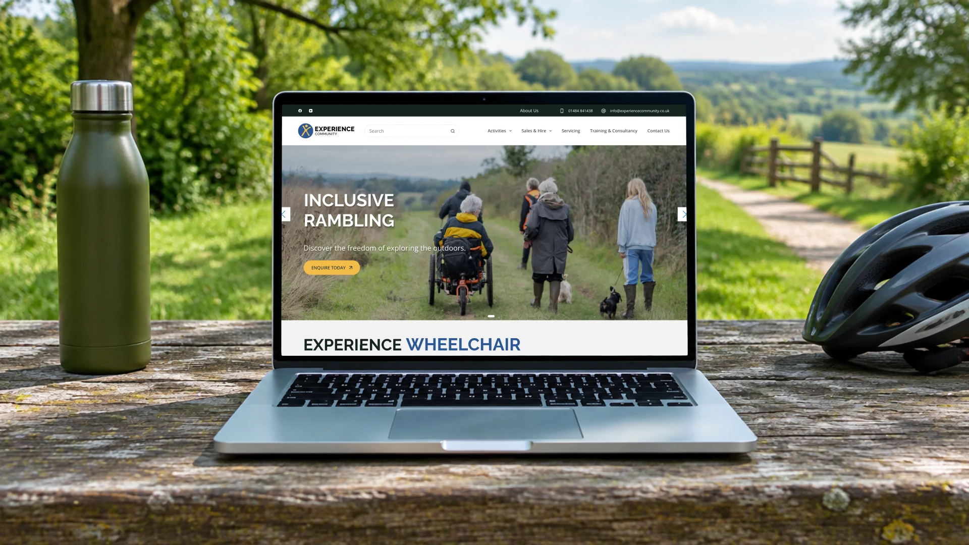 A laptop on a picnic table in a countryside park, showing the Experience Community homepage with its inclusive rambling photography