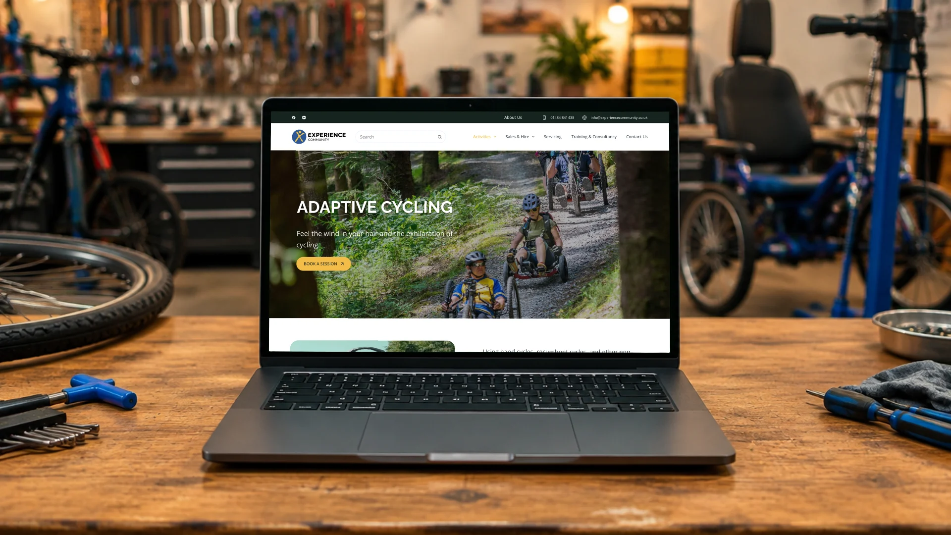 A laptop on a bike workshop bench showing the Experience Community adaptive cycling page